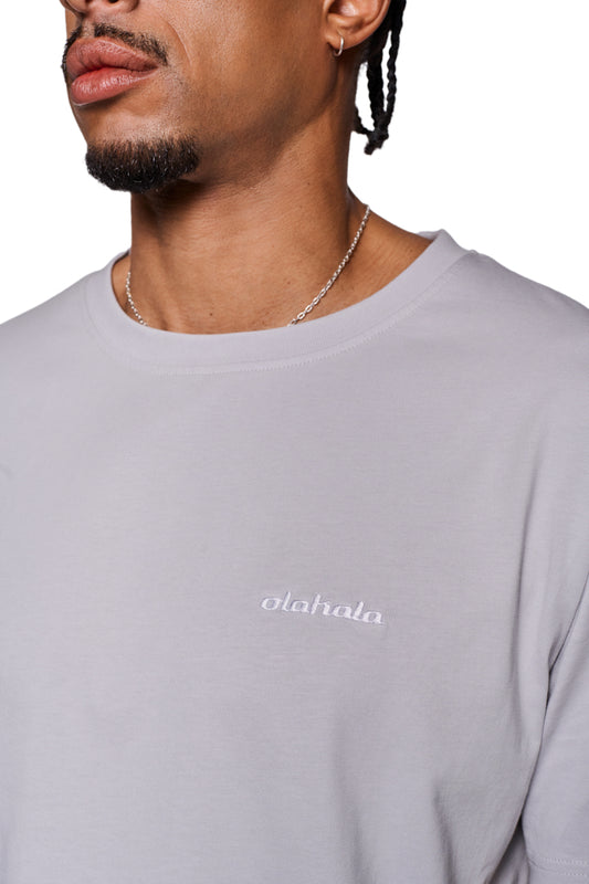 Mann trägt CC T-Shirt Regular Grau mit gesticktem OLAKALA-Logo auf der linken Brust, ripp-Kragen und regulärer Passform. Unisex-Design.