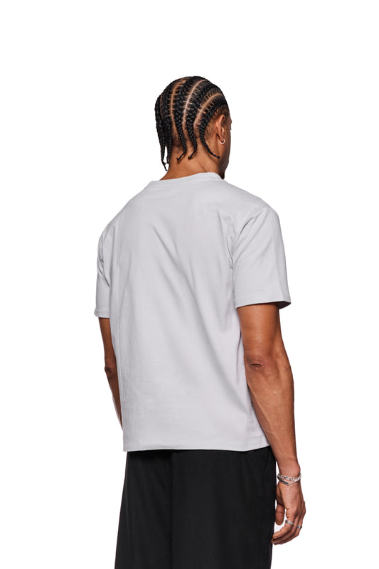 Mann mit Zöpfen trägt ein weißes Isolation T-Shirt mit Ripp-Kragen und Siebdruck-Grafik, reguläre Passform, unisex, präsentiert von OLAKALA.