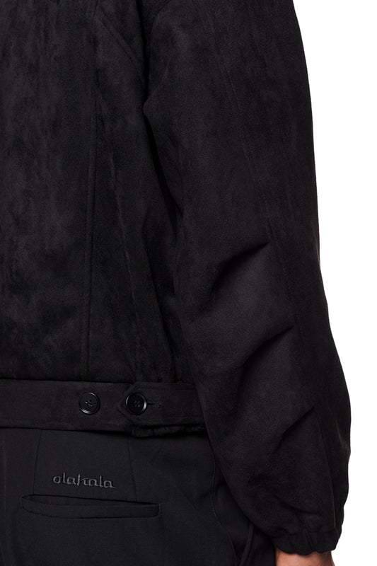 Nahaufnahme der CC Anatomy Velour Jacket Black mit doppeltem Kragen, asymmetrischem Rücken und elastischen Bündchen, zeigt Paspeltaschen und gesticktes OLAKALA Logo.