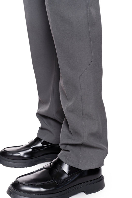 Schlanke CC Dress Pants mit asymmetrischen Taschen und Bundfalten, gezeigt mit schwarzen Schuhen; gesticktes OLAKALA-Logo über der rechten Gesäßtasche.