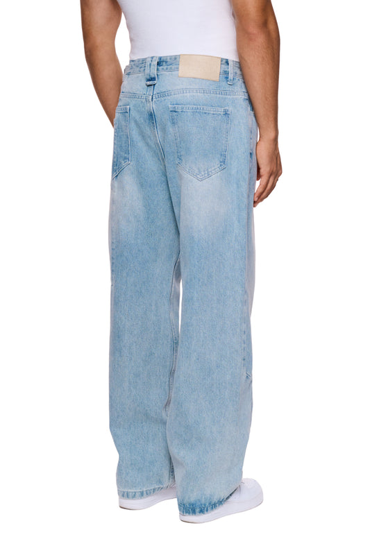Person trägt CC Denim Pants Regular Blue mit versetztem Hosenbund und gesticktem OLAKALA Logo. Zeigt 5-Pocket-Design und geprägtes Patch am Bund.