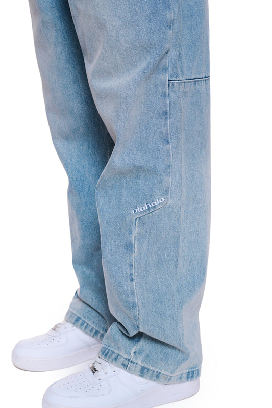 Person trägt CC Denim Pants Regular Blue mit versetzter Seitennaht und gesticktem OLAKALA Logo, kombiniert mit weißen Sneakers.
