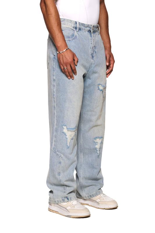 Person trägt Distressed Denim Pants von OLAKALA mit Used-Look, hinterlegten Patches, versetztem Bund und Mittelfinger-Patch an der Gürtelschlaufe.