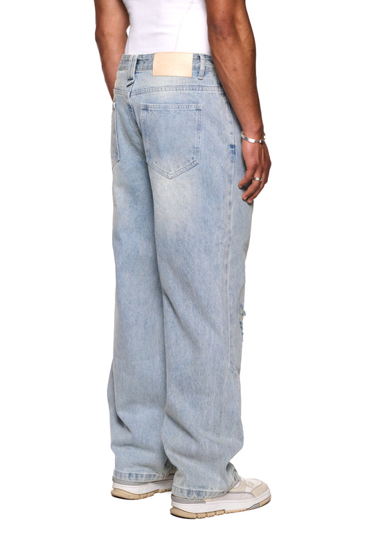 Person trägt Distressed Denim Pants mit versetztem Hosenbund und gesticktem OLAKALA Logo. Sichtbare Patches und „Mittelfinger“ Patch an Gürtelschlaufe.