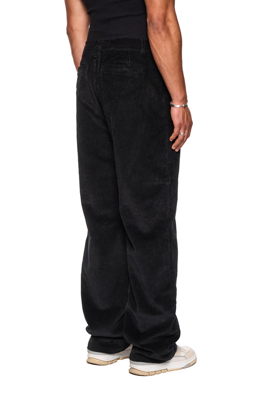 Person wears OLAKALA corduroy pants black with asymmetric pockets, embroidered logo and regular fit, presented in the official OLAKALA® online store.