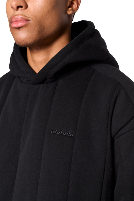 Nahaufnahme des Greyzone Puffer Hoodies mit gesticktem OLAKALA Logo auf der Brust, gepolstertem Design und Oversized-Passform, ideal für modische Unisex-Trends.