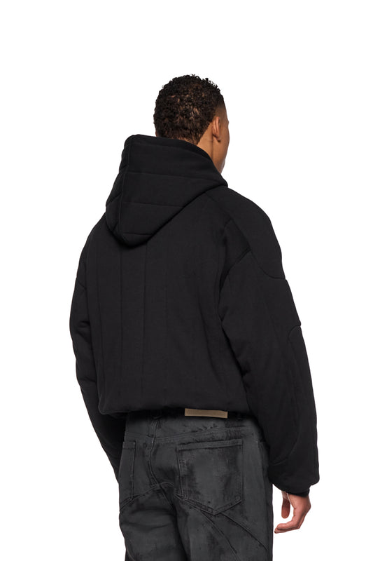 Person trägt den Greyzone Puffer Hoodie von OLAKALA mit gesticktem Logo, gepuffertem Design, Ripp-Bündchen und elastischem Saum in Oversized-Passform.