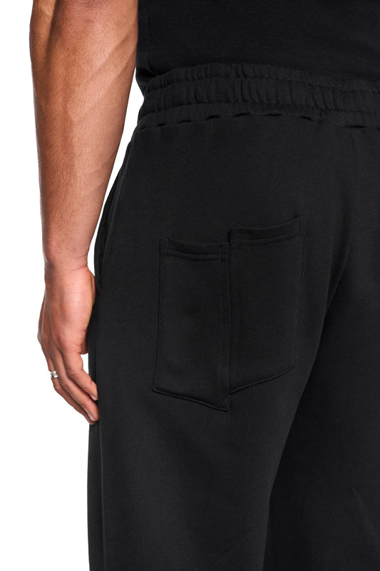 CI Loose Sweatpants Black mit asymmetrischen Taschen und elastischem Bund, Nahaufnahme einer Gesäßtasche und eines Seitennähte-Reißverschlusses.