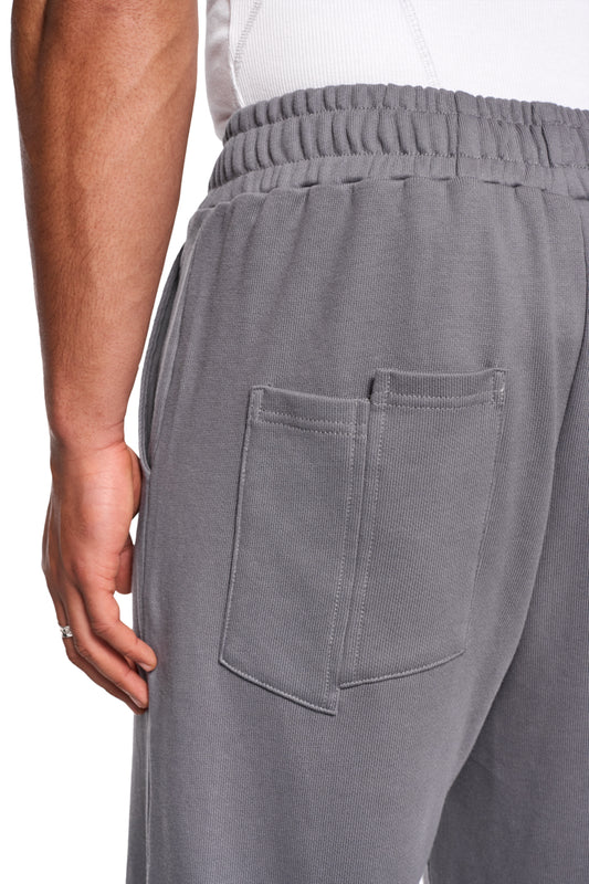 CI Loose Sweatpants Gray mit asymmetrischen Taschen, elastischem Bund und gesticktem OLAKALA-Logo. Nahtloser Reißverschluss am Saum, lockere Passform, unisex.
