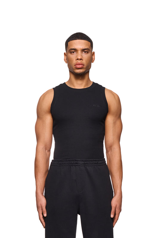 Mann trägt CC Core Tanktop Black aus elastischem Ripp-Stoff mit gesticktem OLAKALA-Icon auf der Brust, zeigt enge Passform.