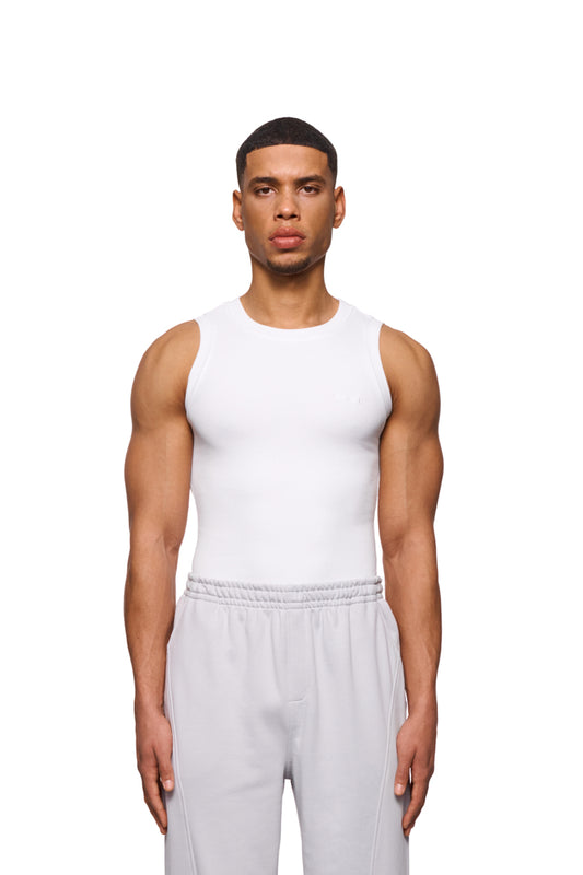 Mann trägt CC Core Tanktop White aus elastischem Ripp-Stoff mit gesticktem OLAKALA-Icon auf der Brust, zeigt enge Passform, unisex Design.