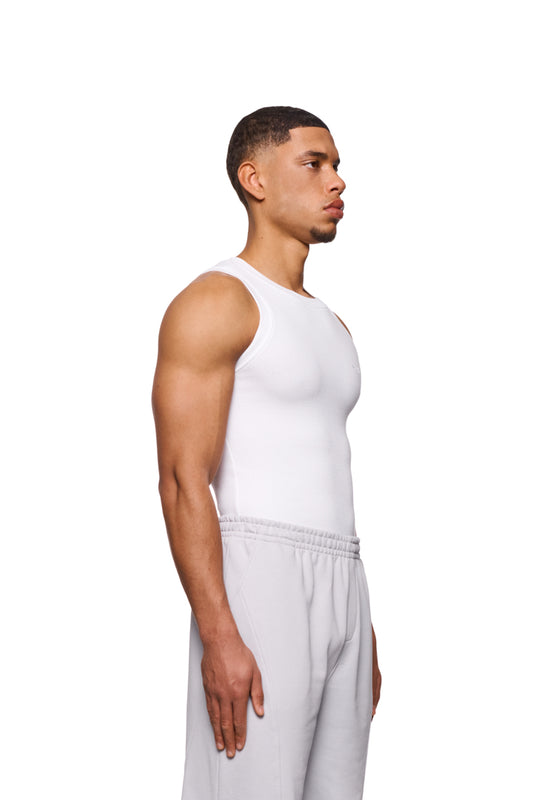 Mann trägt CC Core Tanktop White, betont durch elastischen Ripp-Stoff und gesticktes OLAKALA-Icon auf der Brust, zeigt enge, unisex Passform.