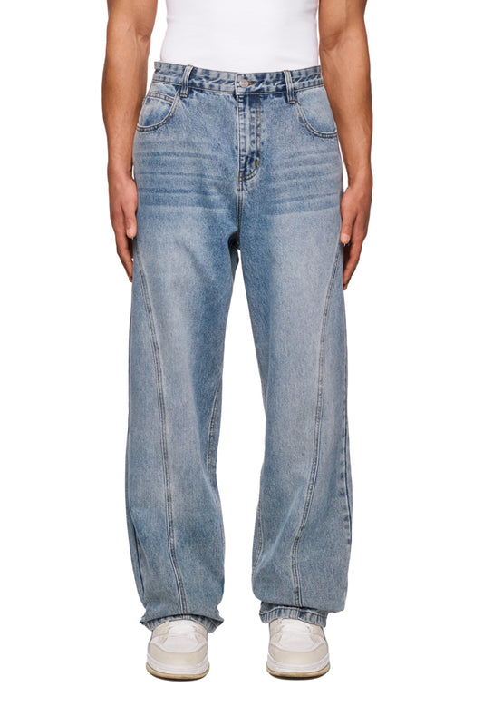 Person wears CC Core Denim Pants Blue, robust jeans with 5-pocket style and washed-out look, white shoes visible.