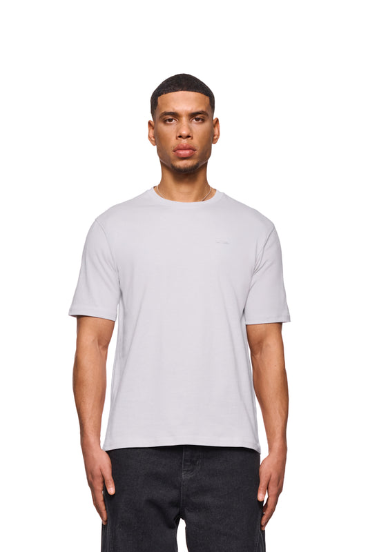 Mann trägt weißes CC Core T-Shirt mit Ripp-Kragen und gesticktem OLAKALA-Icon auf der Brust, reguläre Passform, unisex.