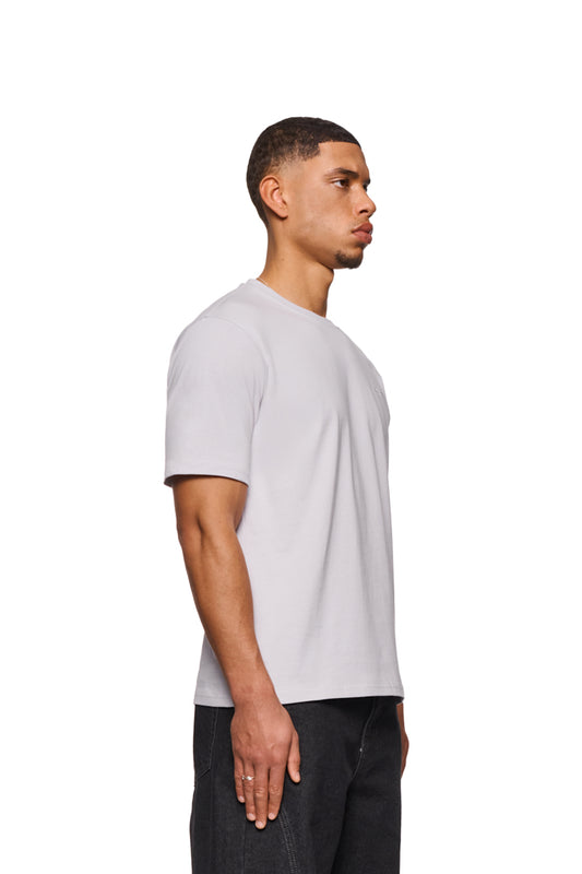Mann im weißen CC Core T-Shirt mit Ripp-Kragen und gesticktem OLAKALA-Icon auf der Brust, präsentiert in regulärer Passform.