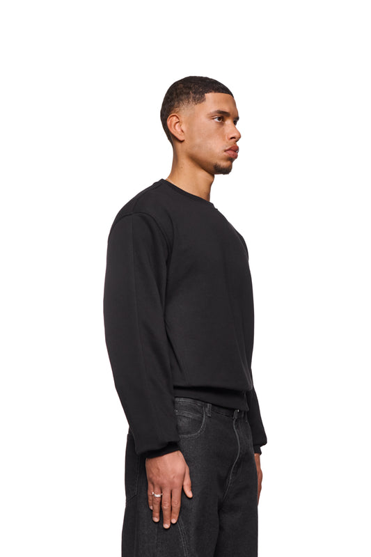 CC Core Sweater Black: Man in black sweater with ribbed cuffs and shifted seams for comfort, regular fit, unisex, durable blended fiber for longevity.