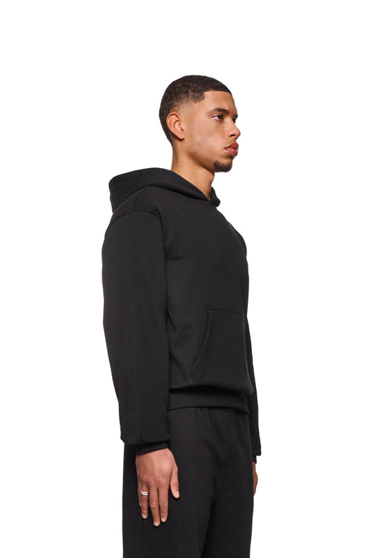 Mann im CC Core Hoodie Black mit Kängurutasche und Rippbündchen, zeigt strapazierfähige Mischfaser und reguläre Passform für erhöhten Tragekomfort.
