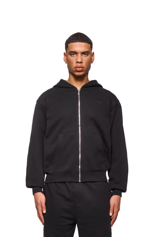 Mann trägt CC Core Zip Hoodie Black mit Kängurutasche und Rippbündchen, bekannt für Langlebigkeit und Komfort, erhältlich im offiziellen OLAKALA® Onlineshop.