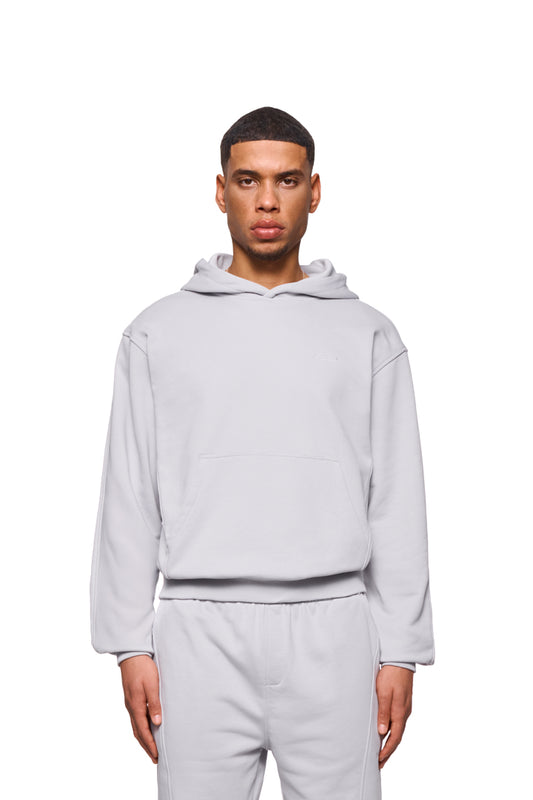 Mann trägt CC Core Hoodie Grau mit Kängurutasche und Rippbündchen, reguläre Passform, betont Komfort durch verlegte Nähte. Unisex-Design von OLAKALA.
