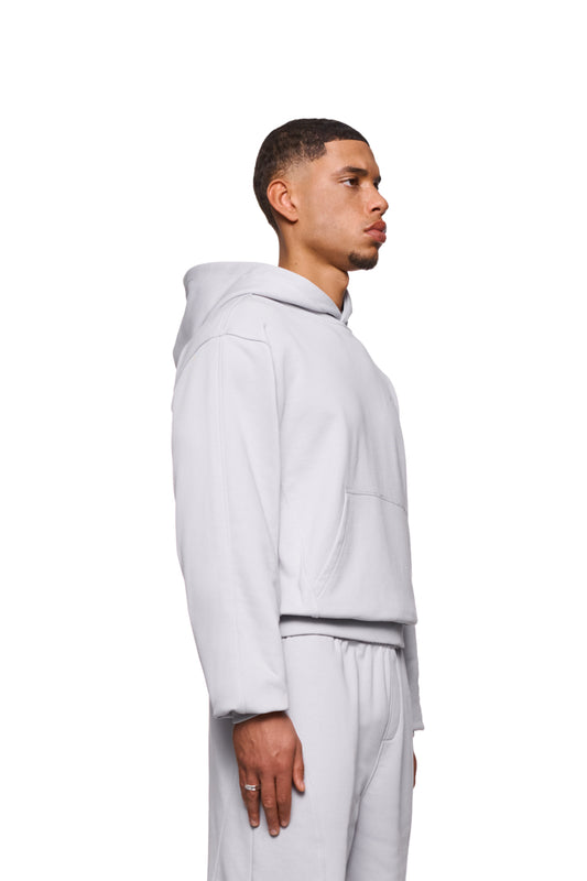 Mann im CC Core Hoodie Grau mit Kängurutasche und Rippbündchen, betont durch strapazierfähige Mischfaser und verlegte Nähte für Komfort. Unisex Design.