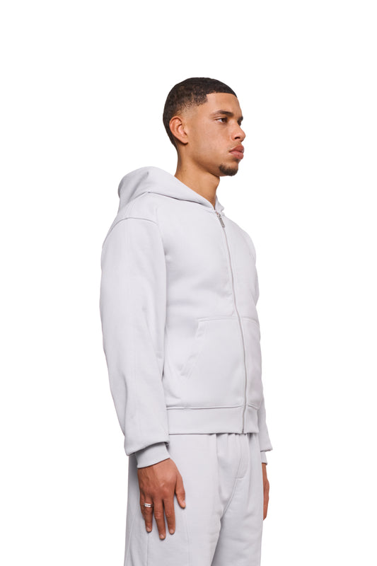 Mann in weißer Jacke zeigt CC Core Zip Hoodie mit Kängurutasche und Rippbündchen, betont Strapazierfähigkeit und Komfort. Unisex, reguläre Passform.