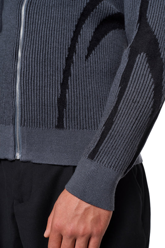 Nahaufnahme eines Arms in einem Luminous Zip Jacket Gray mit hohem Kragen und gestricktem Muster, zeigt elastische Ärmelbündchen und reguläre Passform.