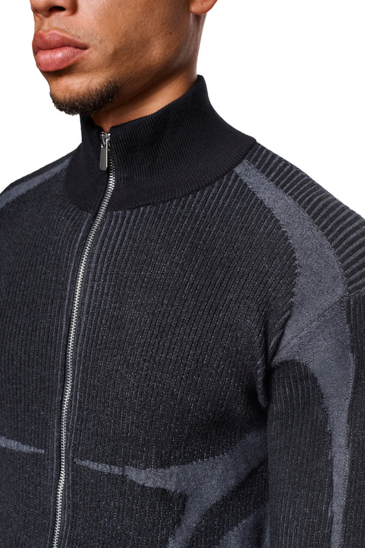 Mann trägt Luminous Zip Jacket Black mit hohem Kragen und gestricktem Muster, Nahaufnahme des Reißverschlusses und Gesichts. Unisex, reguläre Passform.
