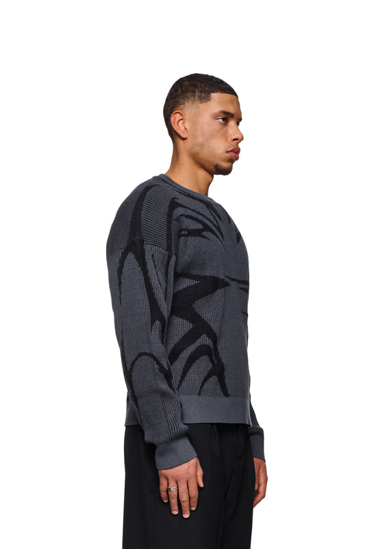 Man wears Luminous Sweater Gray with knitted pattern and elastic cuffs. Loose, unisex cut, presented in the official OLAKALA® online store.