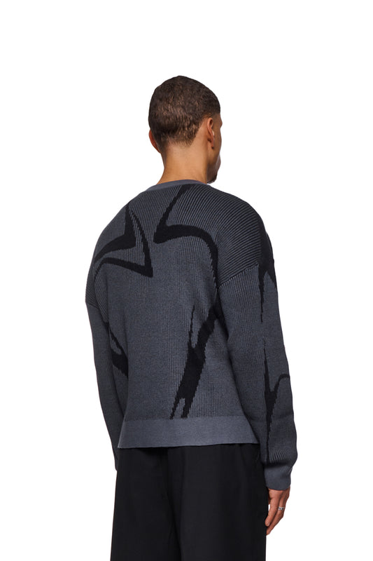 A man wears a gray Luminous Sweater with knitted pattern and elastic cuffs, loose fit, unisex, presented by OLAKALA.