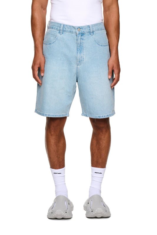 Nahaufnahme der 0asis Denim Shorts Blue mit 5-Pocket-Design, versetzter Passe, aufgesetzter Tasche und OLAKALA Patch, getragen von einer Person mit weißer Socke.