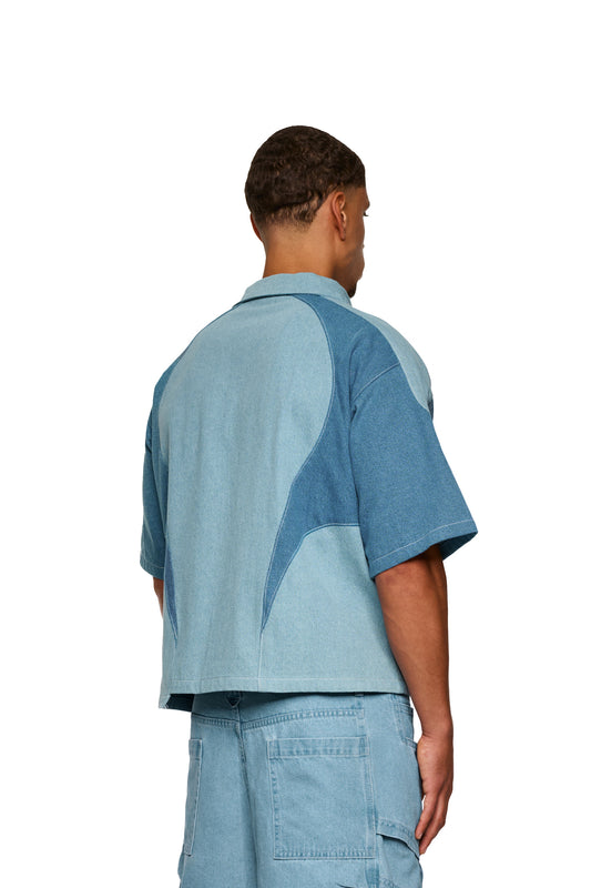 Mann trägt das Echoes Denim Icon Shirt Blau mit kubanischem Kragen, Knopfleiste, Brusttasche mit Logo, kontrastierenden Teilungsnähten und lockerer Passform.