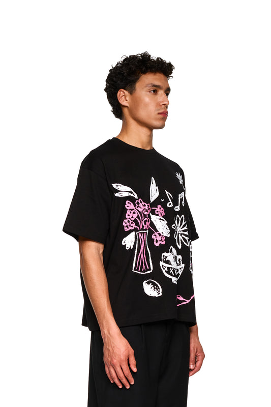 Nahaufnahme eines Mannes in einem schwarzen Crayon T-Shirt Oversized von OLAKALA, fokussiert auf das Design und die Passform der Ärmel.