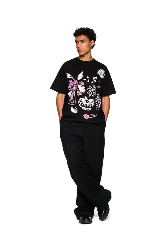 Mann trägt ein Crayon T-Shirt Oversized in Schwarz, stehend. Konzentriert sich auf das lässige Design und die Passform des OLAKALA® Produkts.