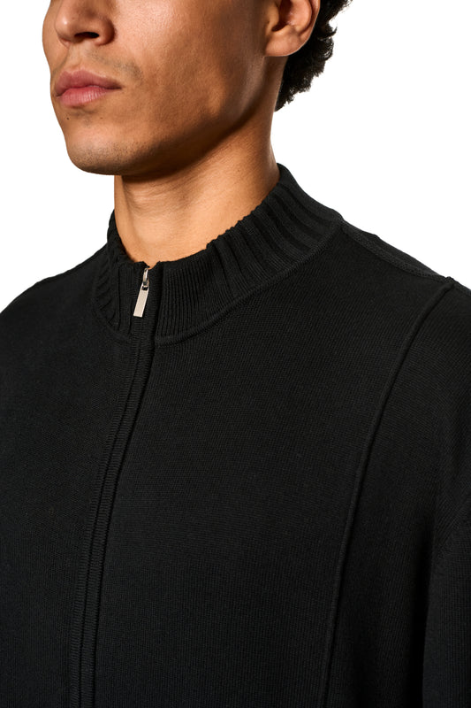 Nahaufnahme eines Mannes, der die Sommer-Strickjacke Schwarz mit asymmetrischer Vorderseite und Metallreißverschluss trägt, ideal für warme Sommerabende.