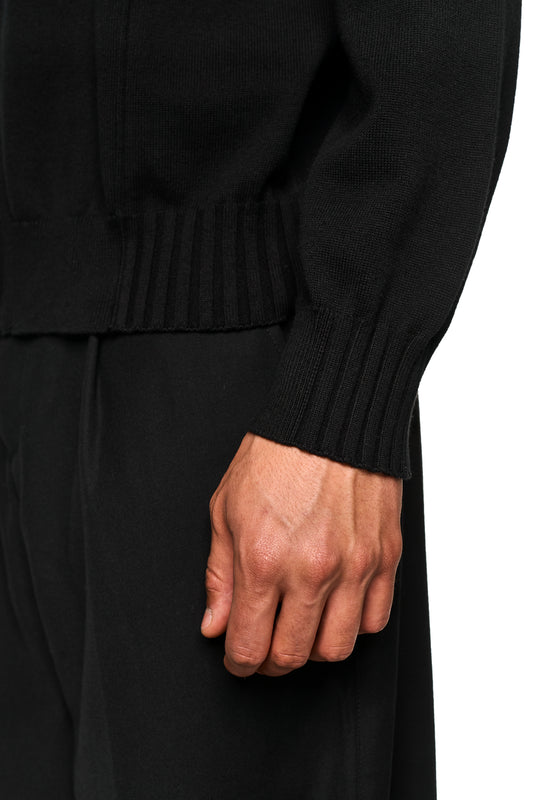 Nahaufnahme einer Hand, die die feine Struktur der Summer Knit Jacket Black mit asymmetrischer Vorderseite und sichtbaren Inside-Out-Nähten am Kragen zeigt.
