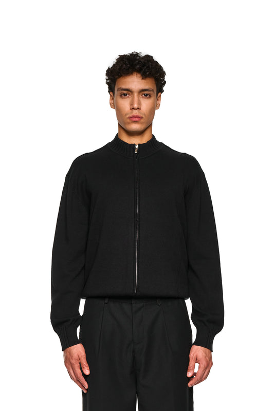 Nahaufnahme der Summer Knit Jacket Black mit asymmetrischer Vorderseite, weichem Baumwollstrick im Rippenmuster und Inside-Out-Nähten, gezeigt an einem stehenden Modell.
