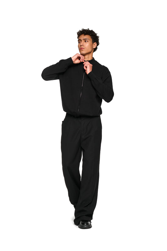 Mann in schwarzer Sommer-Strickjacke mit asymmetrischer Vorderseite und Metallreißverschluss, ideal für warme Abende, präsentiert von OLAKALA.