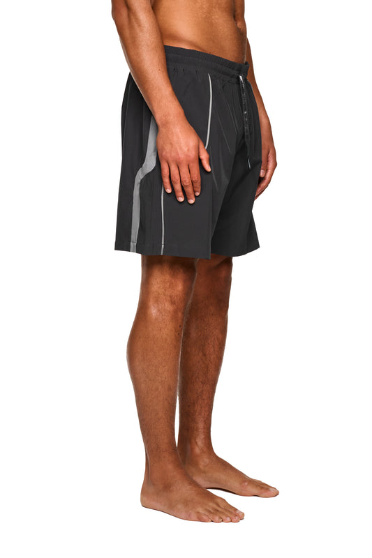 Nahaufnahme eines Mannes, der die 0asis Swim Shorts Gray trägt, mit kontrastierenden Einsätzen, silikonbeschichteten Kordelzügen und einem Logo-Print auf dem linken Bein.