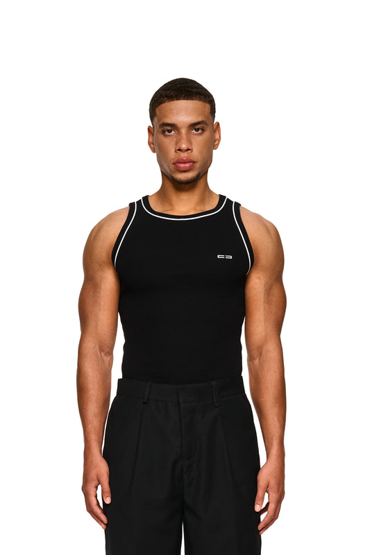 Nahaufnahme eines Mannes im Contrast Tanktop Black mit elastischem Ripp-Stoff und gesticktem OLAKALA Icon auf der linken Brust, betont Schultern und Brustmuskulatur.