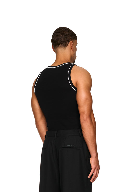 Ein Mann trägt ein eng anliegendes, schwarzes Contrast Tanktop mit elastischem Ripp-Stoff und gesticktem OLAKALA-Icon auf der linken Brust.