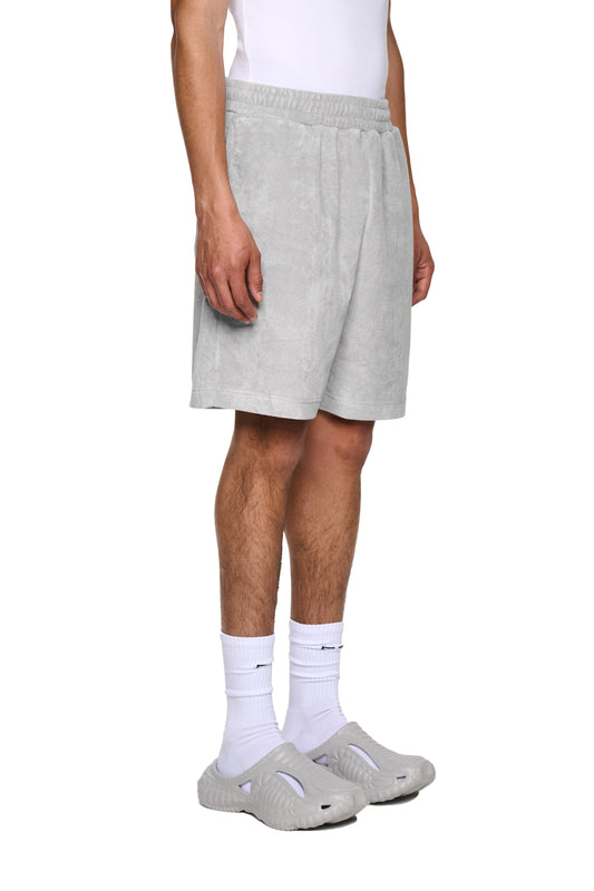 Nahaufnahme einer Hand, die graue Terry Shorts aus weichem Frotteematerial mit elastischem Bund und Kordelzug für optimale Passform präsentiert.