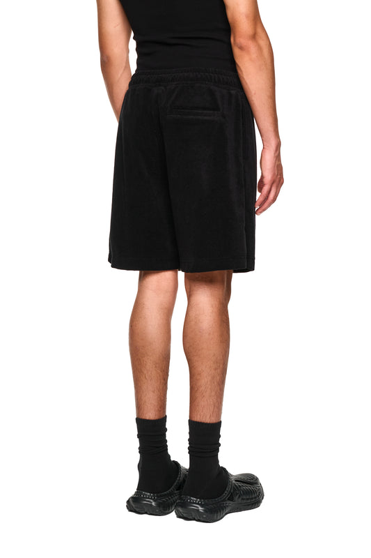 Nahaufnahme von Beinen mit schwarzen Kniestrümpfen und OLAKALA Terry Shorts, aus weichem Frottee mit elastischem Bund und Logo-Stickerei.