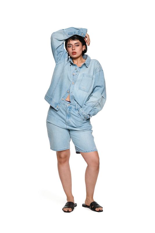 Frau trägt das 0asis Denim Overshirt Blue mit Knopfleiste und geprägtem OLAKALA Patch, zeigt aufgesetzte Brusttaschen und Teilungsnähte.