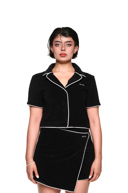 Frau trägt ein schwarzes, strukturiertes Terry Shirt Cropped mit 3D-Monogramm, kontrastierenden Paspelierungen und Logo-Stickerei auf der Brust.