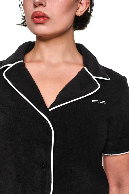 Nahaufnahme eines Gesichts mit Details eines Terry Shirt Black Cropped aus weichem Frottee, 3D-Monogramm-Knopfleiste, kontrastierenden Paspelierungen und Logo-Stickerei auf der Brust.