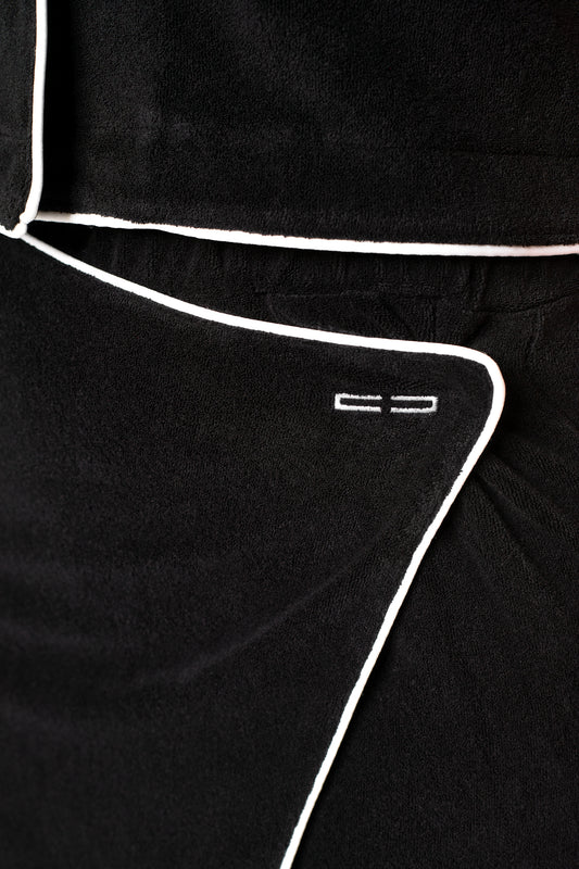 Nahaufnahme des Terry Skort Black: Weiches, strukturiertes Frotteematerial mit Wickelrockdetail und 3D-Monogramm. Elastischer Bund und kontrastierende Paspelierungen.