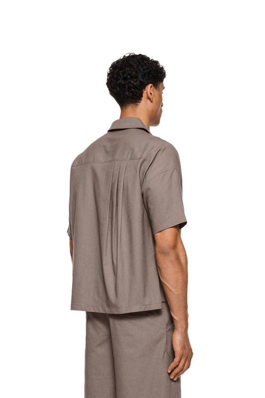 Linen-Kurzarmhemd Beige mit Safari-Kragen, Brusttasche links, Reißverschlüssen vorne und drei Falten hinten. Unisex, reguläre Passform, mit Ton-in-Ton-Logo.