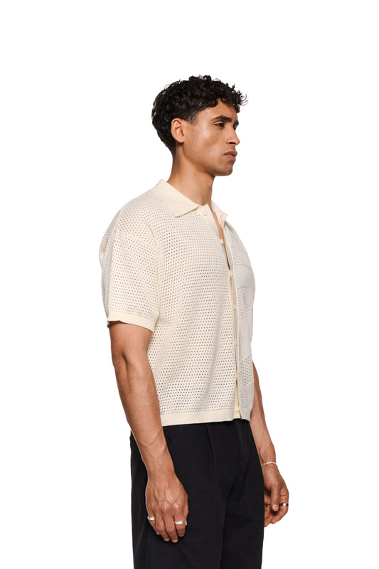 Unisex Sun Knit Shirt Creme mit feinem Lochstrickmuster, Sonnendetail, doppellagigem Kragen, Knopfleiste und lockerer Passform, ideal für warme Sommertage.
