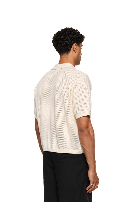 Sun Knit Shirt Creme mit feinem Lochstrickmuster, lockerem Schnitt, Sonnendetail vorne links, doppellagigem Kragen rechts und Knopfleiste in der vorderen Mitte. Unisex.