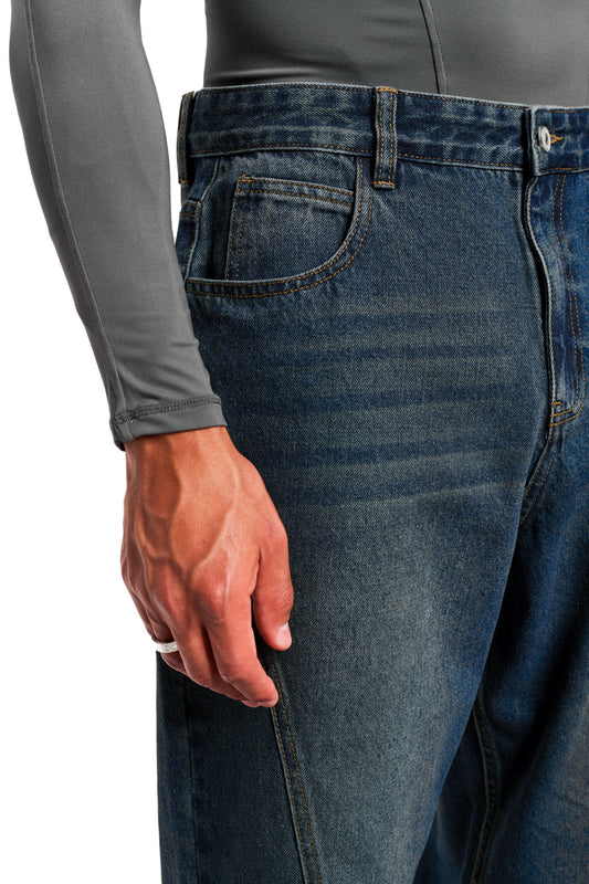 Person trägt CC Core Denim Pants Tinted Indio mit klassischem 5-Pocket-Stil, mittlerer Leibhöhe und charakteristischen Nähten, kombiniert mit einem grauen Langarmshirt.